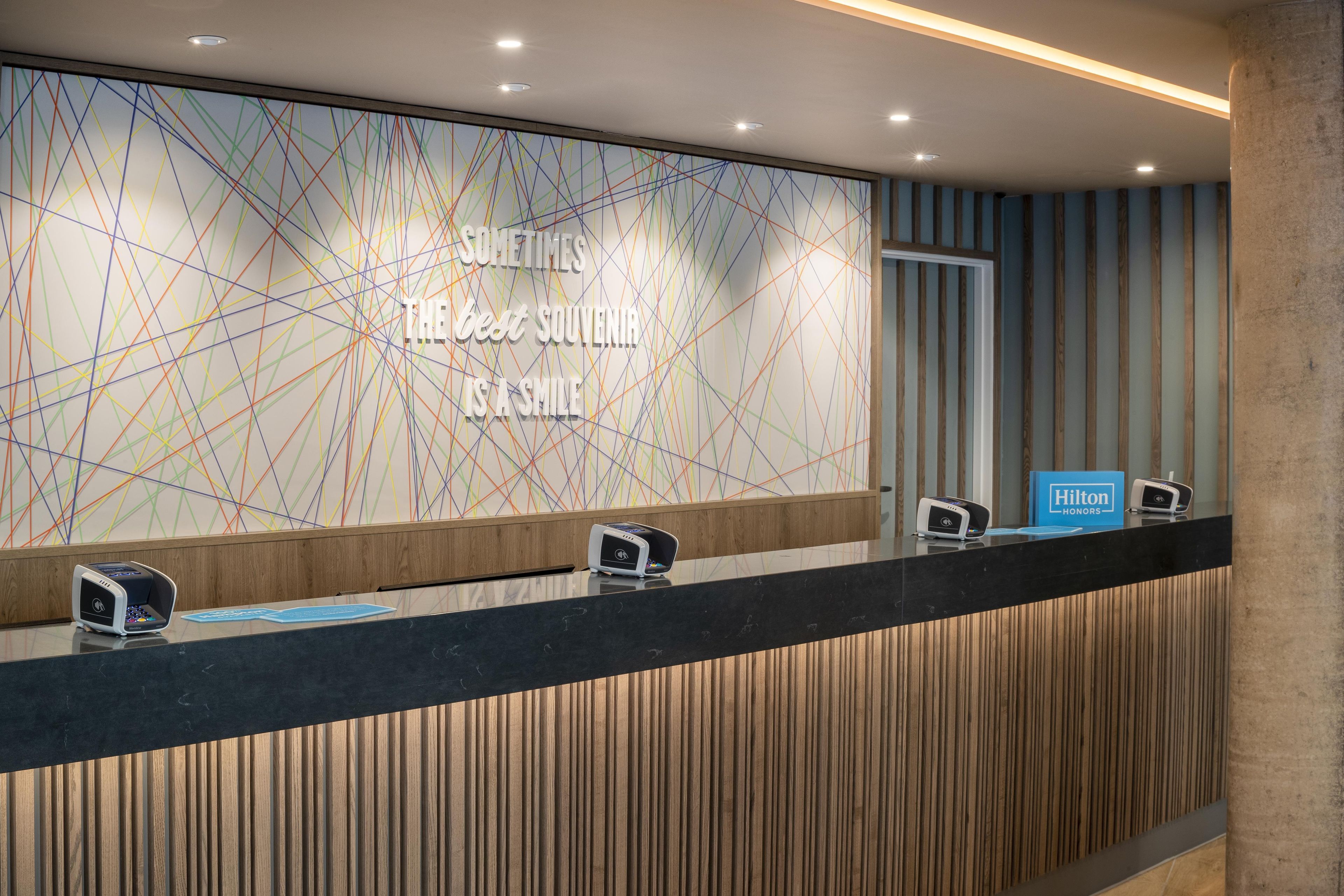 Ein moderner Hotelrezeptionstresen, eine Wandmitte mit Schriftzug und ein blaues Schild mit dem Hotelnamen.