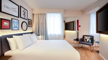 Una habitación de hotel moderna con una cama grande, televisión, zona de estar y obras de arte en las paredes.