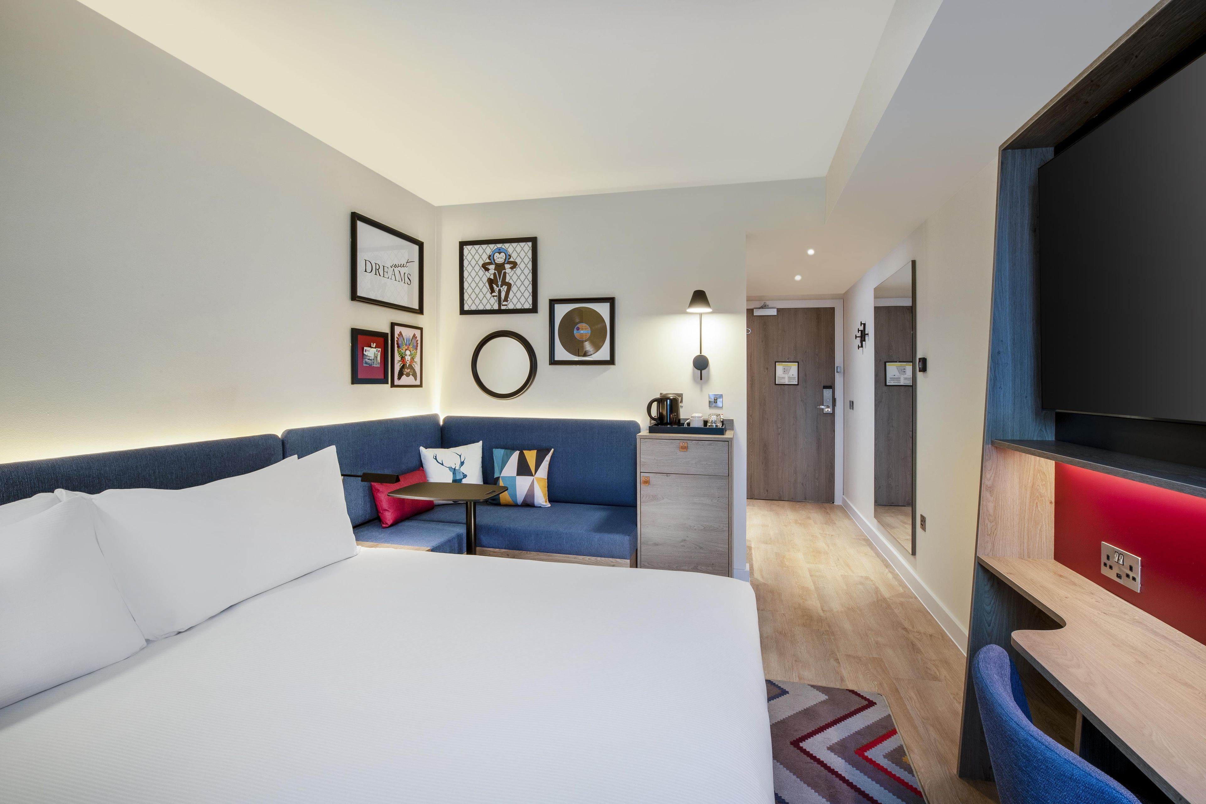 A hotel room with a bed, a sofa, a desk, and a TV.