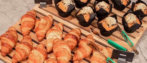 Mostrador de una panadería con distintos productos horneados, como cruasanes y muffins, dispuestos sobre tablas de madera.