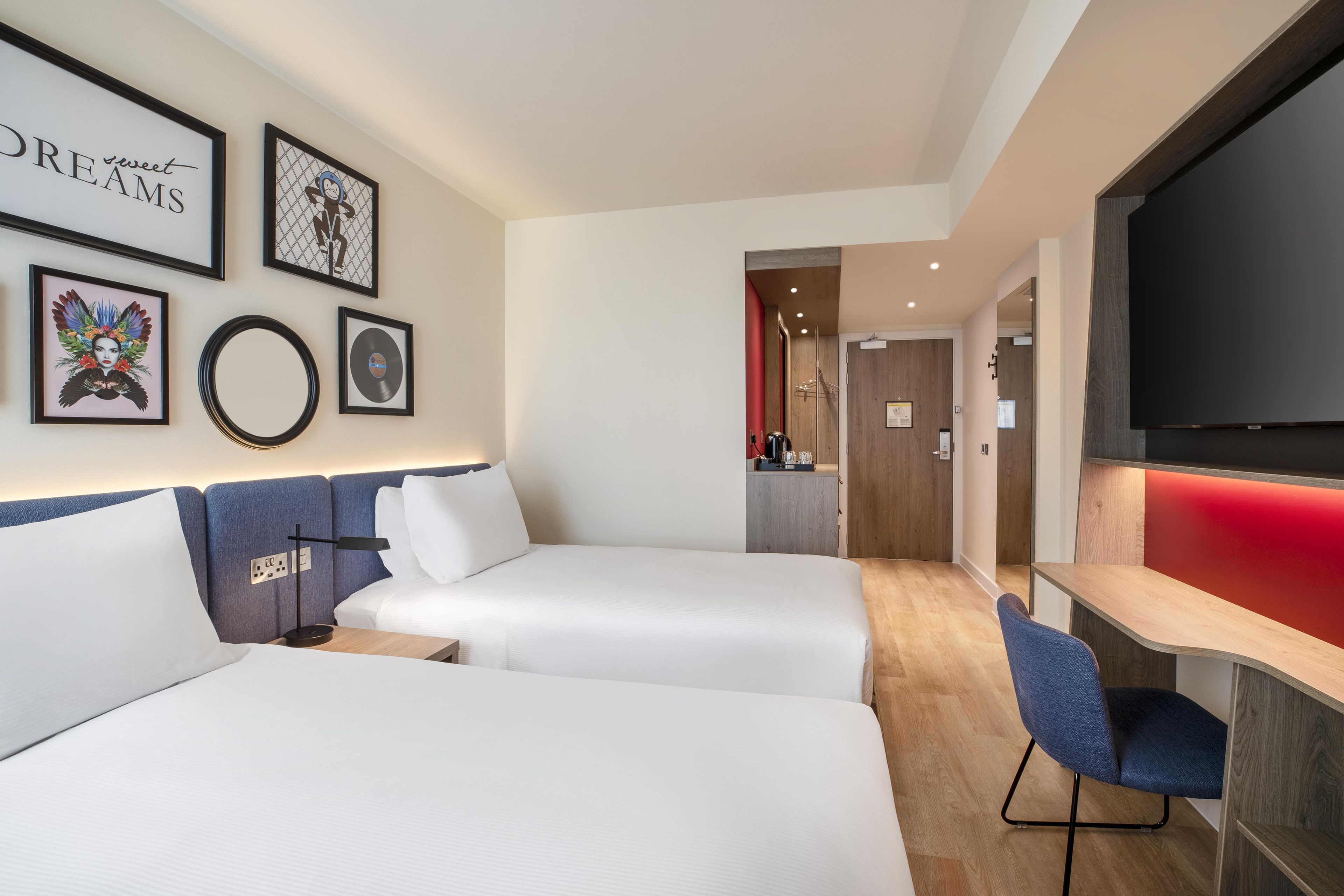A hotel room with two beds, a desk, a chair, and a TV.