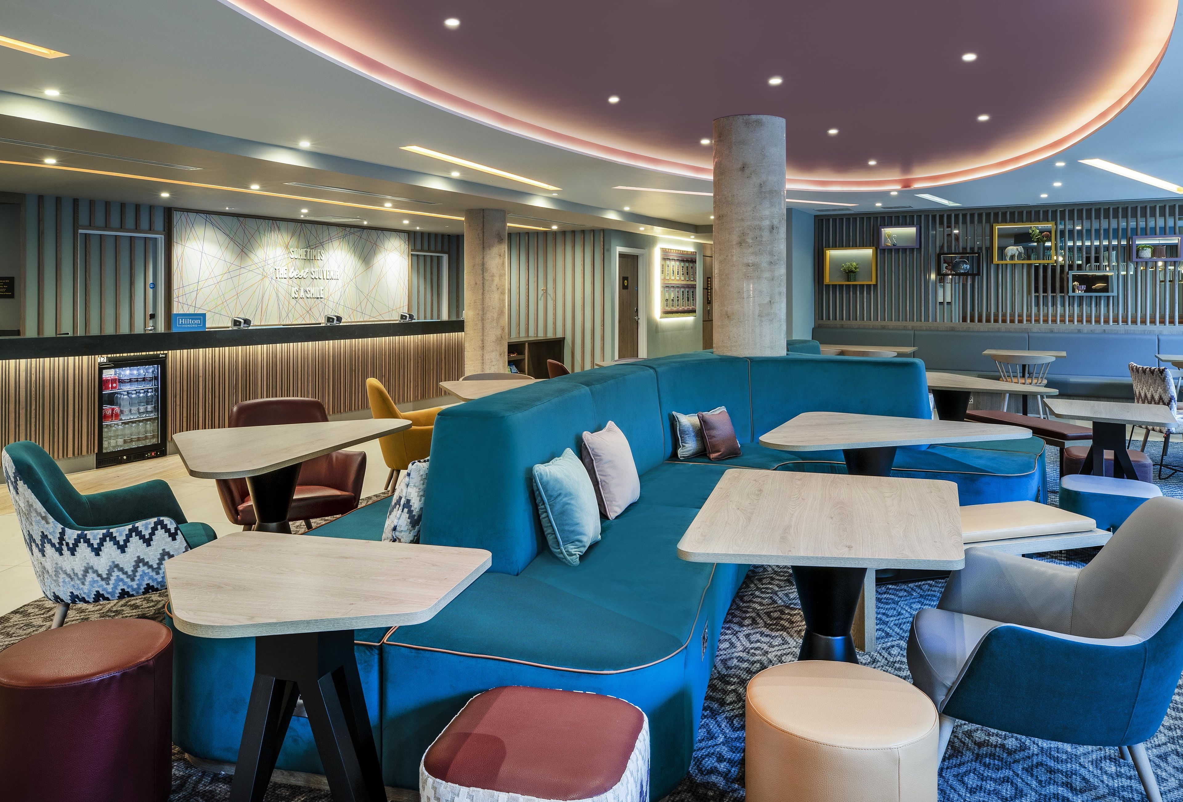 A modern hotel lobby with a blue sofa, round tables, and a bar area.