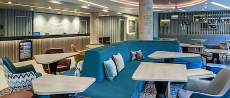 A modern hotel lobby with a blue sofa, round tables, and a bar area.