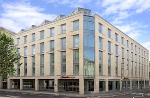 Un edificio en esquina con varios pisos, amplias ventanas y un escaparate visible con un letrero.