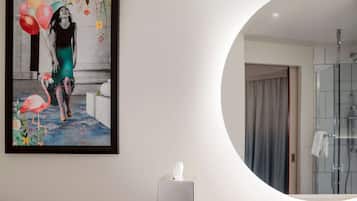 A modern bathroom with a glass shower, a white towel on the wall, and a framed artwork above the sink.