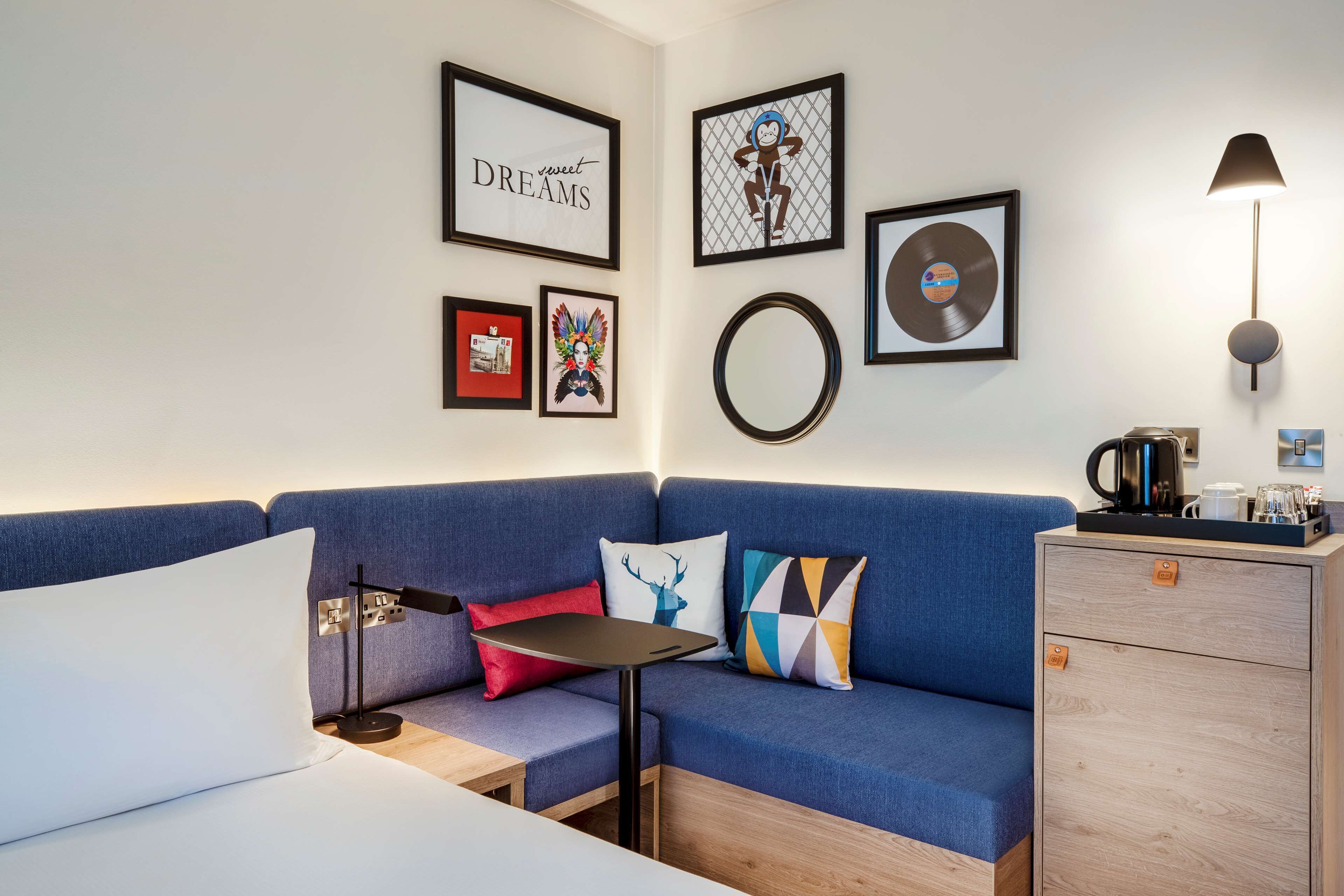 A modern room with a blue sofa, a small table, a cabinet, and wall art including framed pictures and a vinyl record.