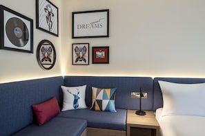 Una sala de estar moderna con un sofá azul, almohadones decorativos, obras de arte enmarcadas y una lámpara de pared.