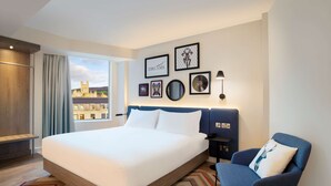 Una habitación de hotel moderna con una cama grande, un sillón azul y vistas a la ciudad.
