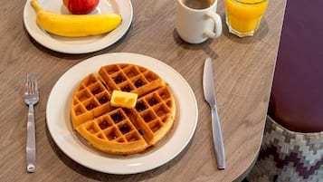 A breakfast setting with a plate of waffles, a banana, an apple, a cup of coffee, and a glass of orange juice.