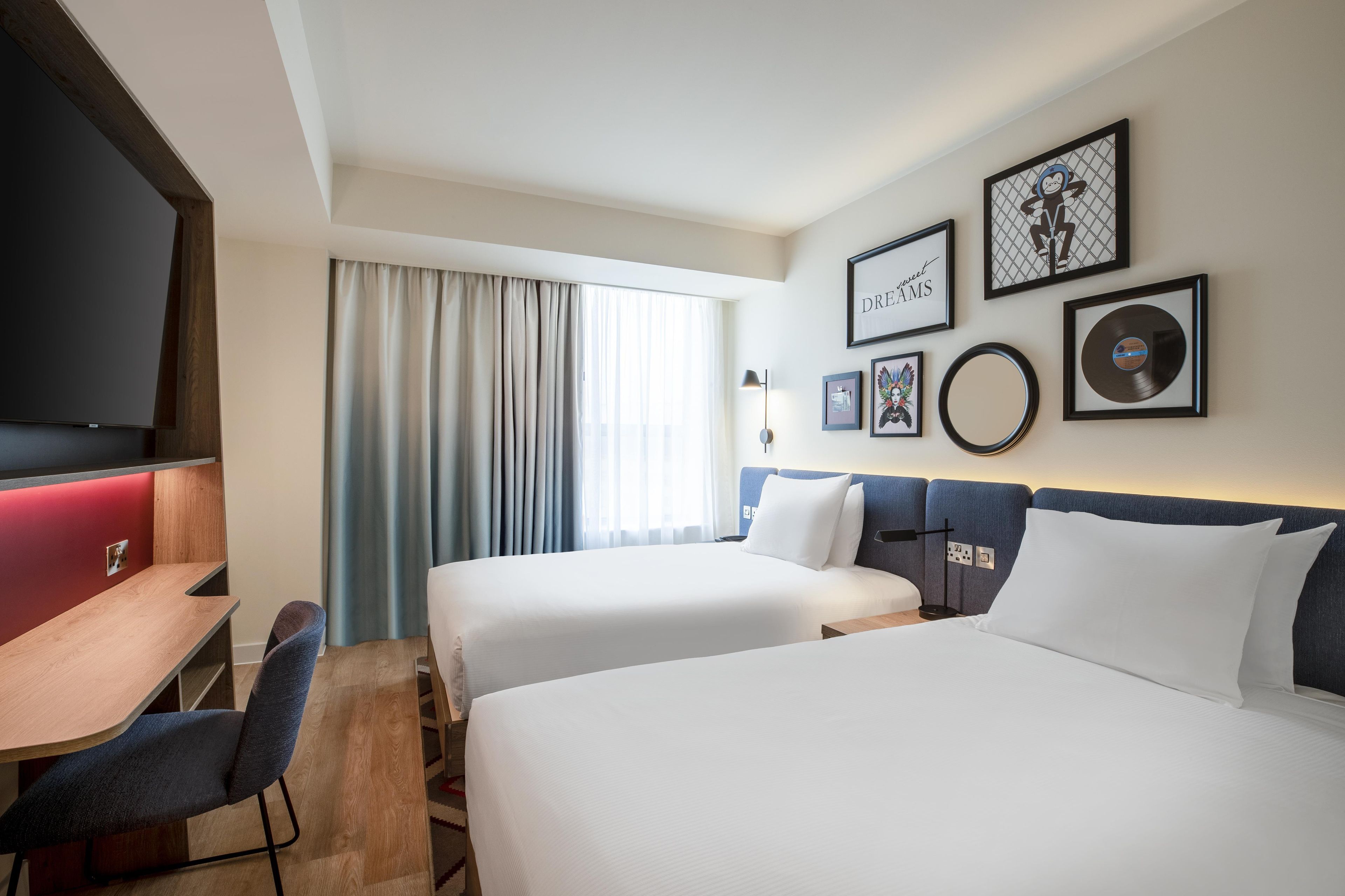 A hotel room with two beds, a desk, a chair, and a TV.