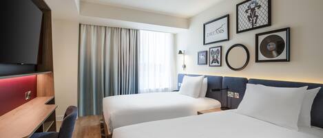 A hotel room with two beds, a desk, a chair, and a TV.