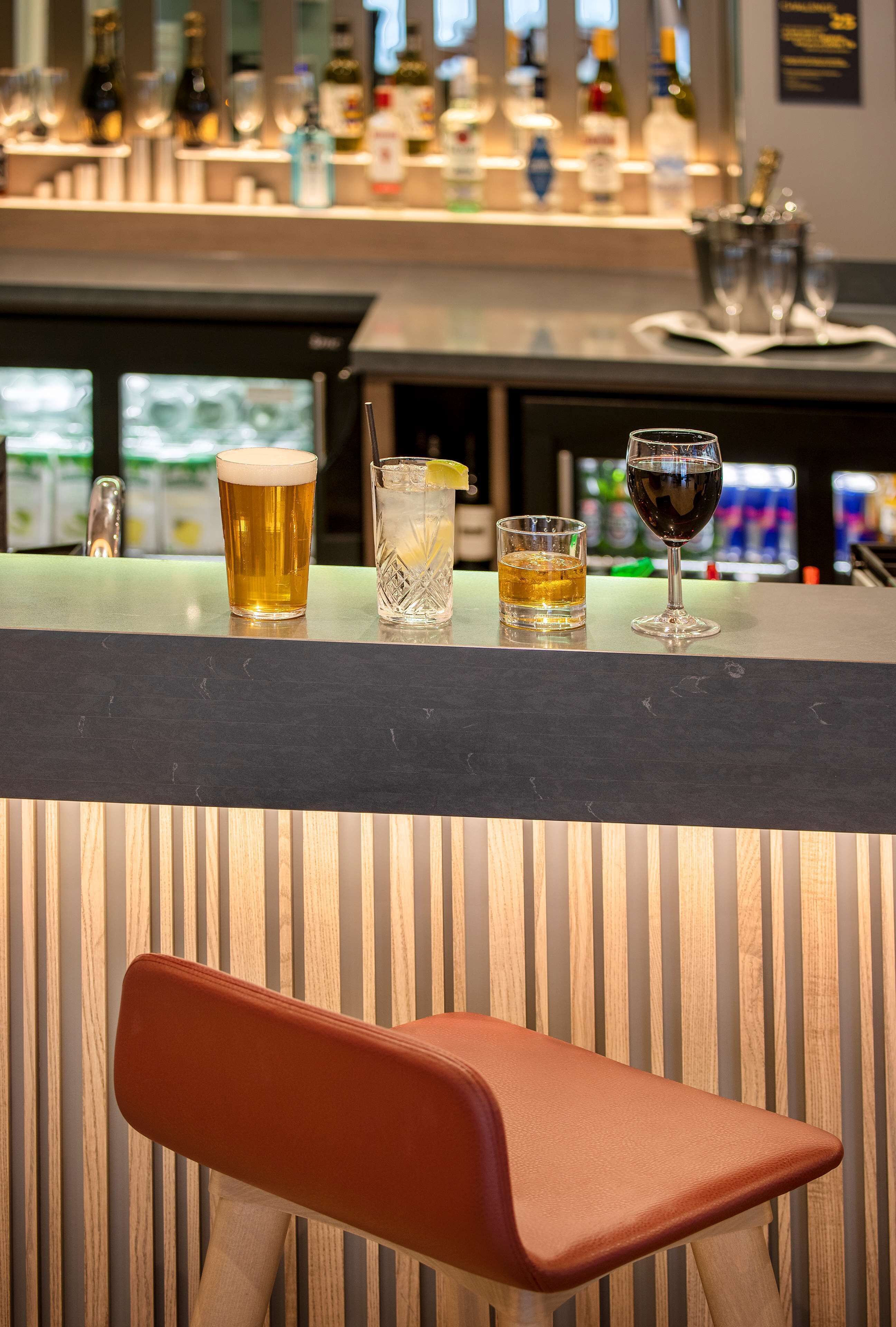 Un espace bar avec un comptoir où sont exposées différentes boissons, et un tabouret au premier plan.