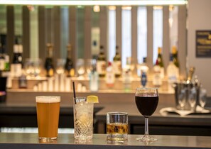 A bar with three glasses of different beverages, a bottle of liquor, and a bar counter. - Hampton by Hilton Bath City (Bath)