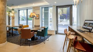 Un moderno vestíbulo de hotel con zona de comedor, ventanas amplias y un escritorio con ordenador.