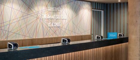 A hotel reception desk with a modern design, a message on the wall, and a sign for Hilton Honors.