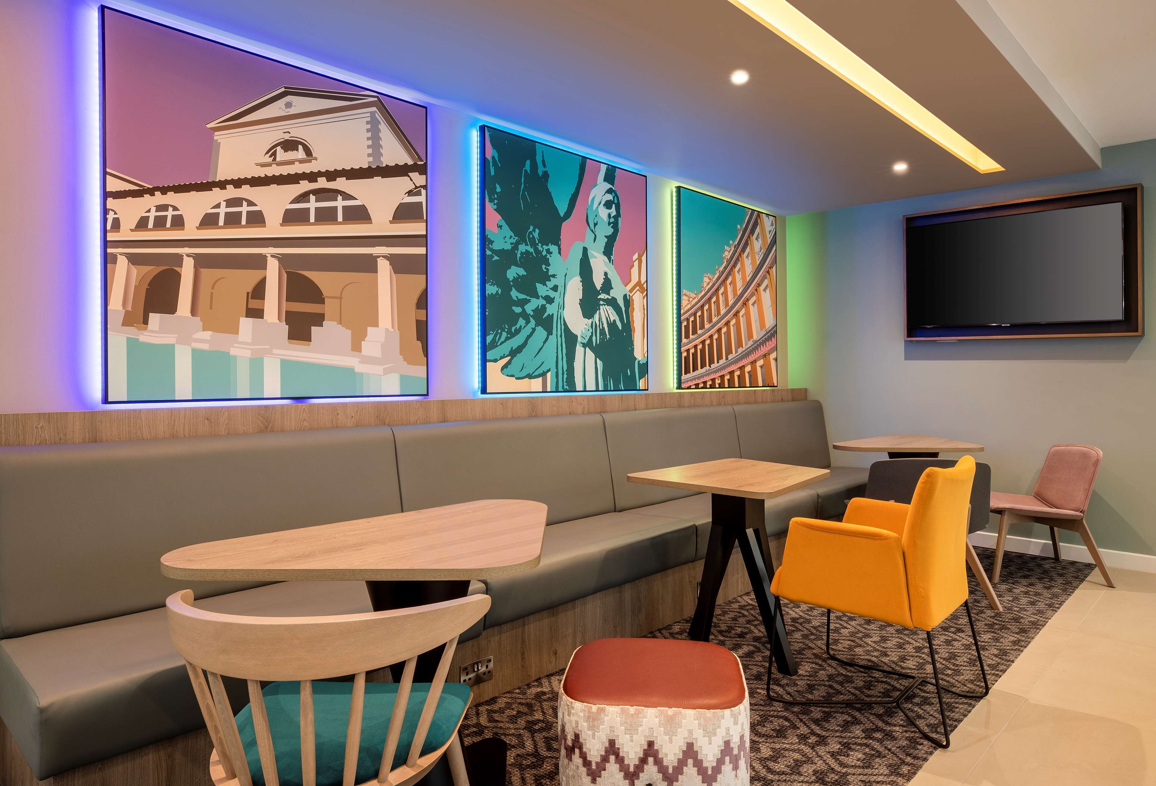 A modern lounge area with a sofa, wooden tables, and colorful artwork on the walls.