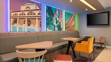 A modern lounge area with a sofa, wooden tables, and colorful artwork on the walls.