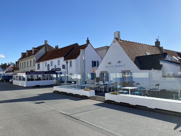 Une rangée de bâtiments blancs, avec un restaurant appelé « LA MARIE GALANTE » et une enseigne sur laquelle on peut lire : « Un petit bonheur ! »