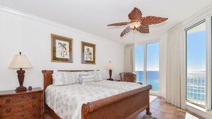 Ein Schlafzimmer mit einem großen Bett, zwei Nachttischen, einem Deckenventilator und Blick aufs Meer.
