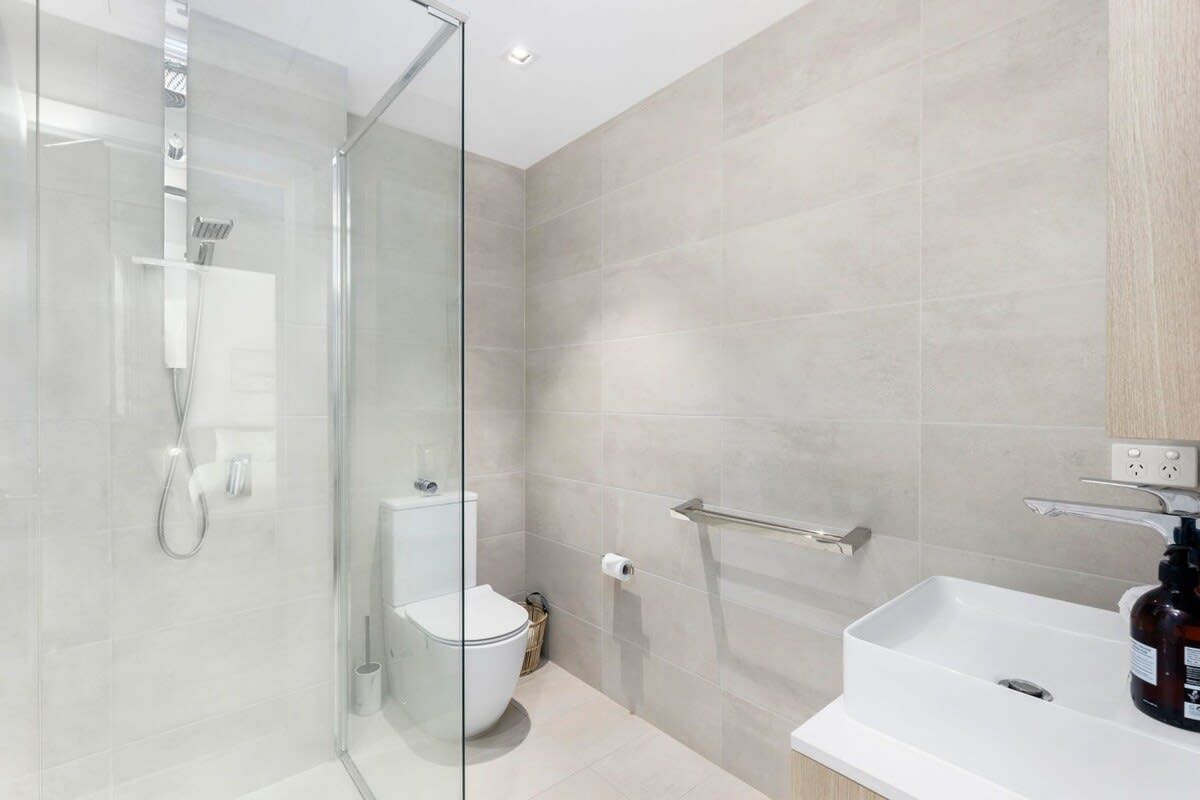 A modern bathroom with a glass shower enclosure, a white sink, and a toilet.