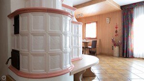 Una stanza con pavimento piastrellato bianco, un tavolo da pranzo in legno con sedie, una panca bianca e una finestra con tenda colorata.