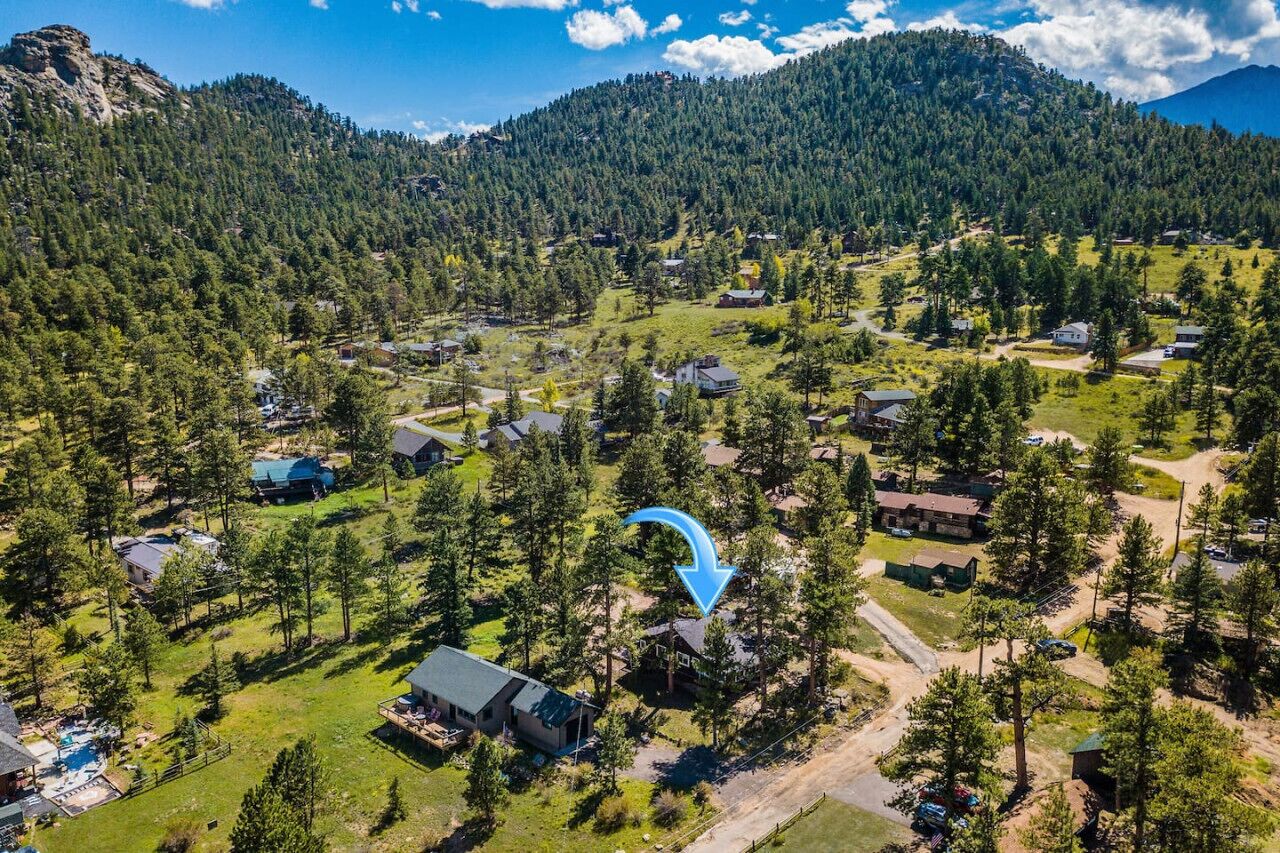 An aerial view of a residential area with houses surrounded by dense forest and mountains.