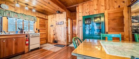 A wooden cabin interior with a kitchen, dining area, and a visible bathroom.