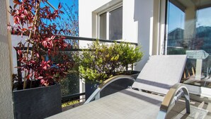 A balcony with a chair, a potted plant with red leaves, and a window. - -DALIA- APPARTEMENT CENTRE-VILLE-TERRASSE-PARKING (Concarneau)