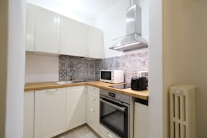 A compact kitchen with white cabinets, a microwave, an oven, and a coffee maker on the countertop. - Vin Novo Rooms & Apartments (Florence)
