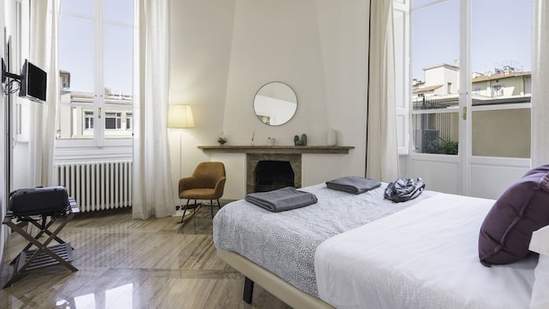 Una habitación de hotel con cama, una silla, chimenea y televisor.
