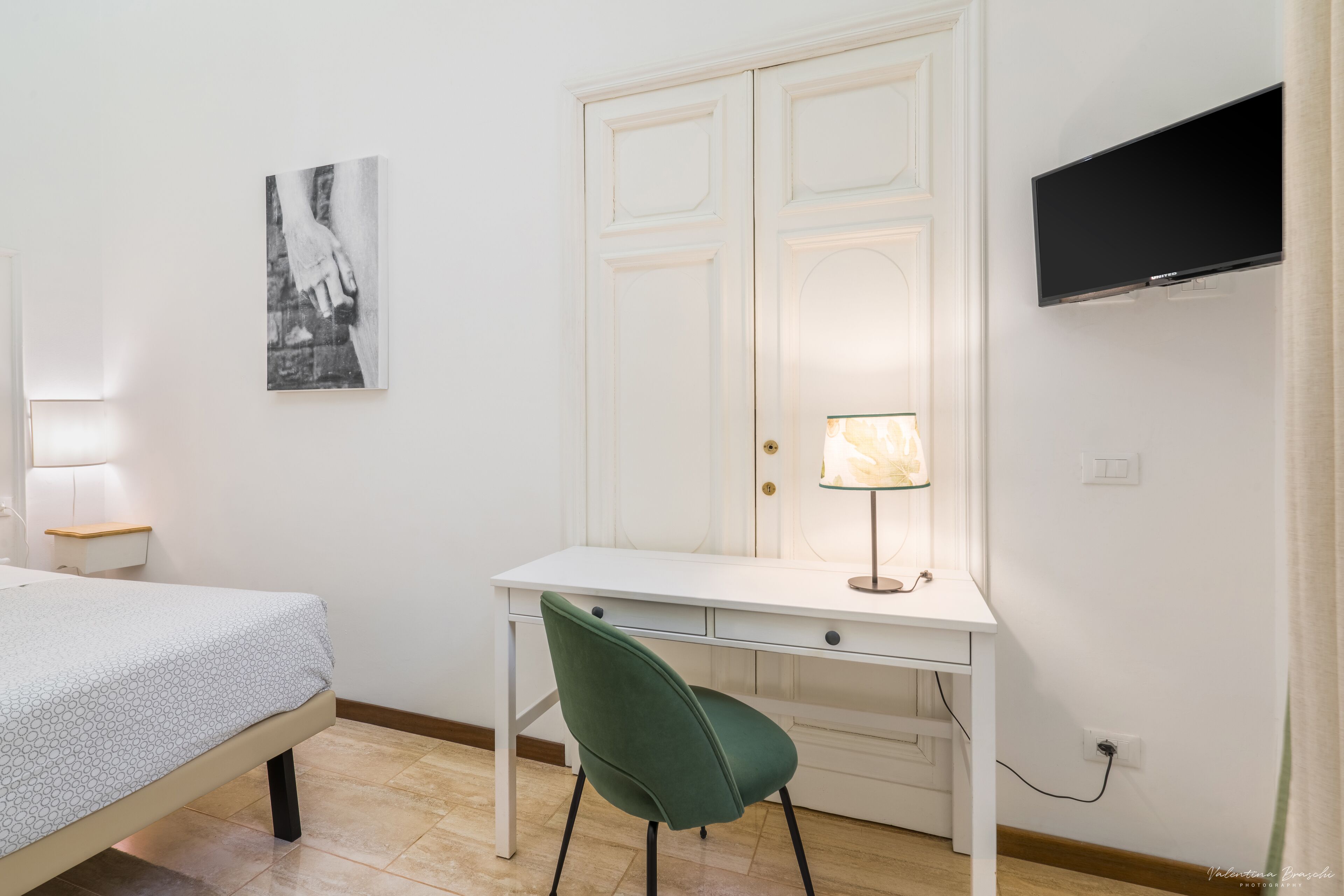Een slaapkamer met een bed, een bureau, een stoel, een televisie en een lamp.