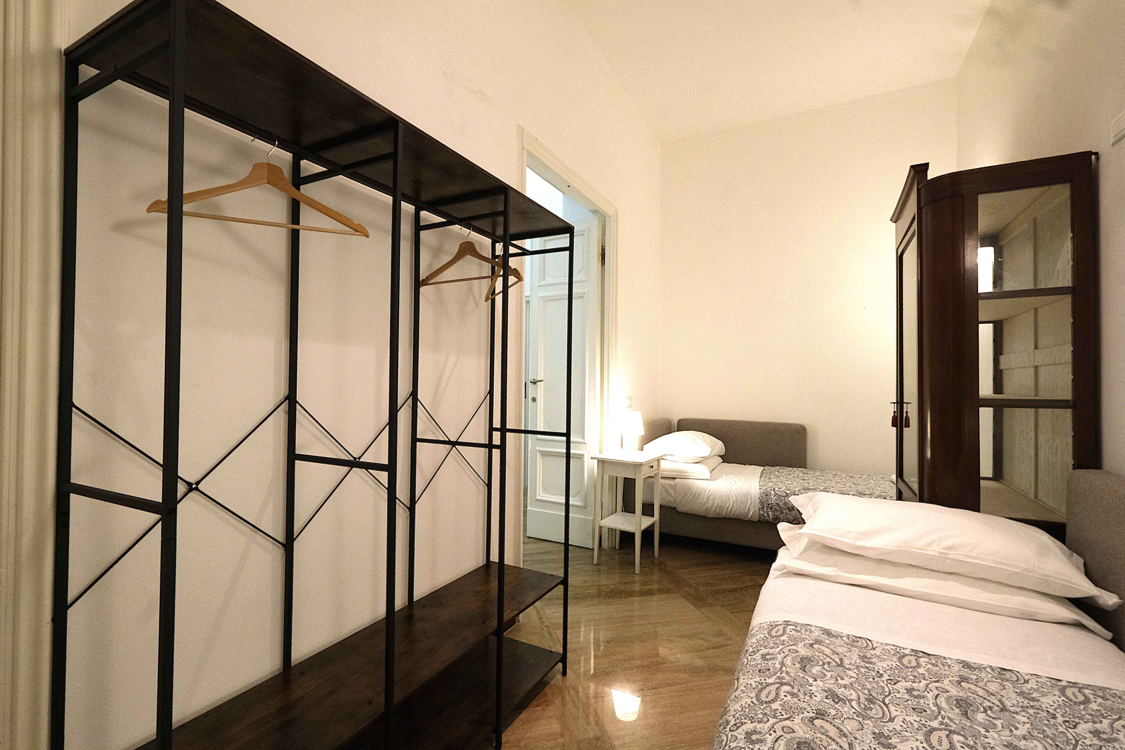 A bedroom with a bed, a bedside table, a hanging wardrobe, and a mirror.