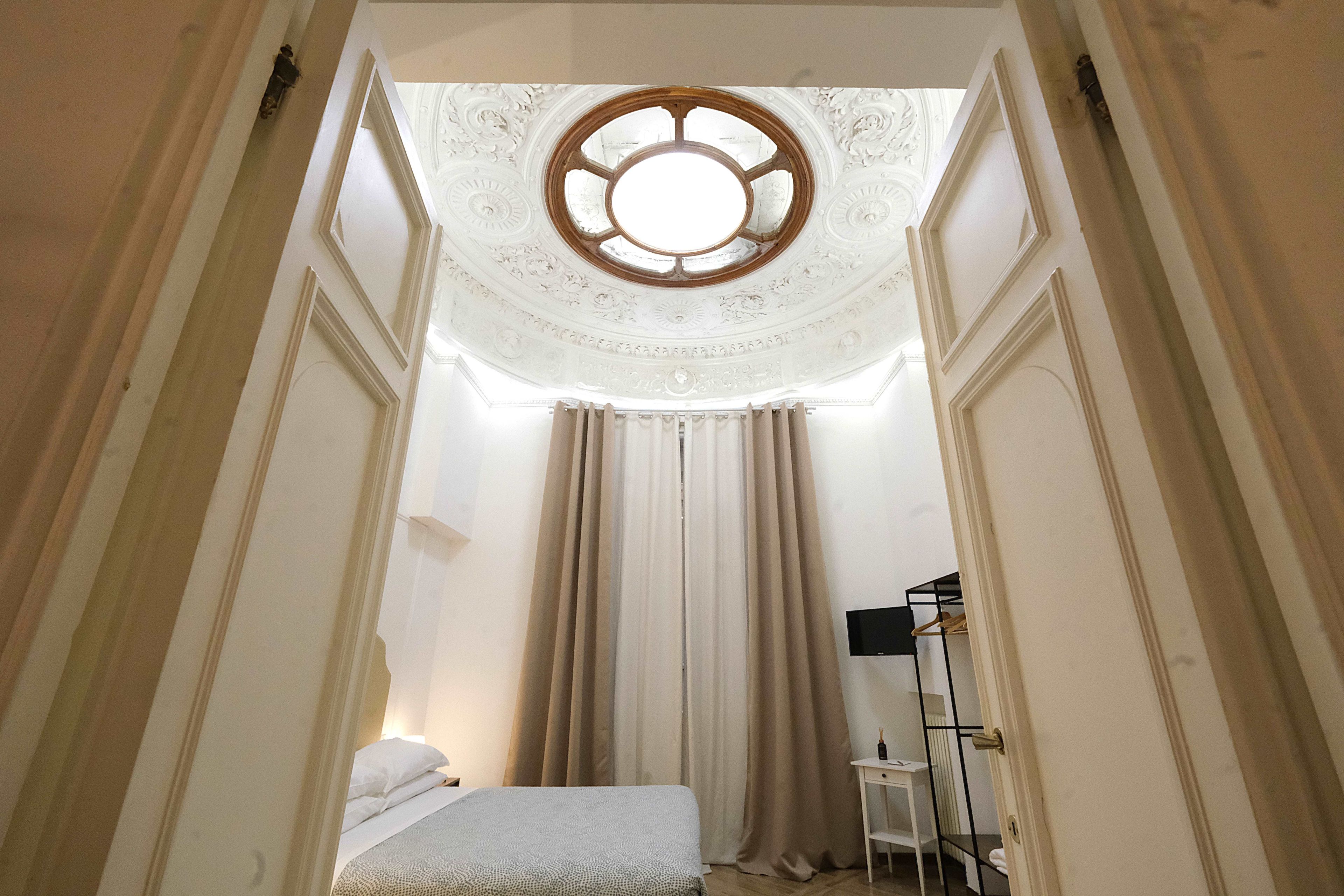 A narrow room with a bed, a window with a wooden frame, and a radiator.