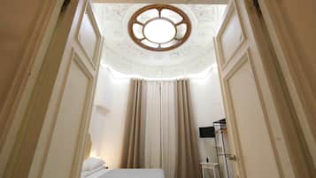 Una habitación estrecha con una cama, una ventana con marco de madera y un radiador.