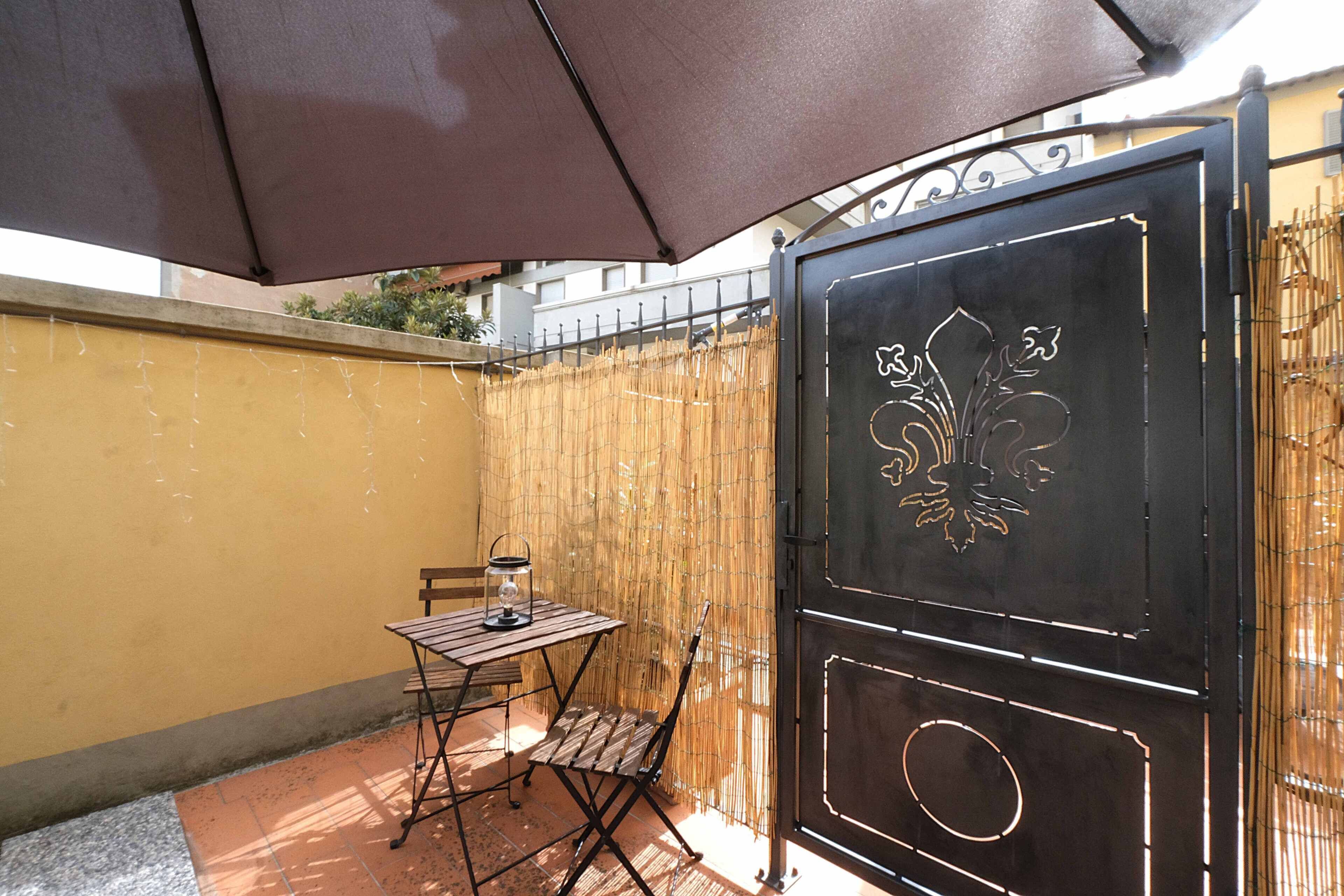 An outdoor patio with a table and chairs, a decorative metal gate, and a bamboo fence.