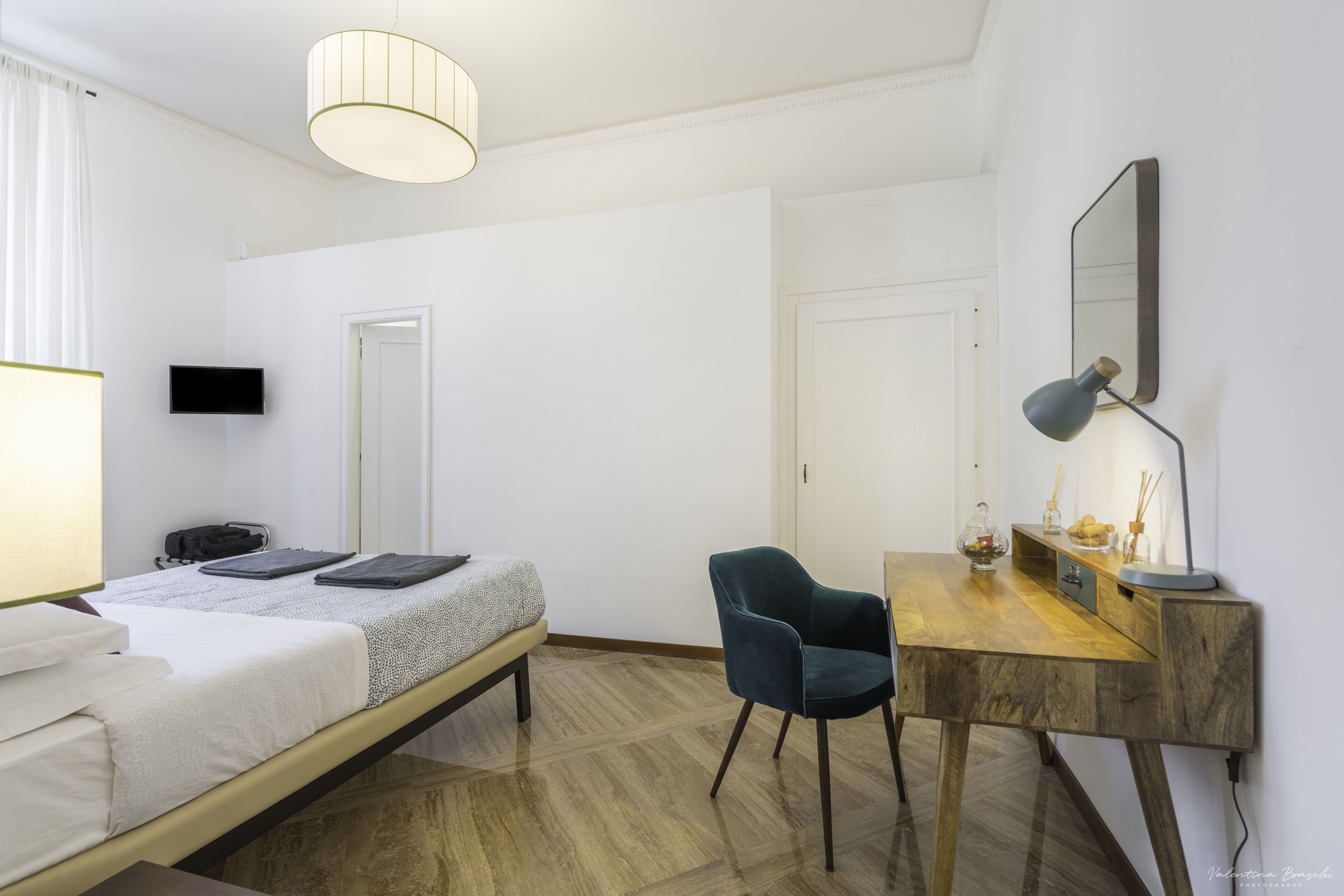 A hotel room with a bed, a desk, a chair, a TV, and a mirror.