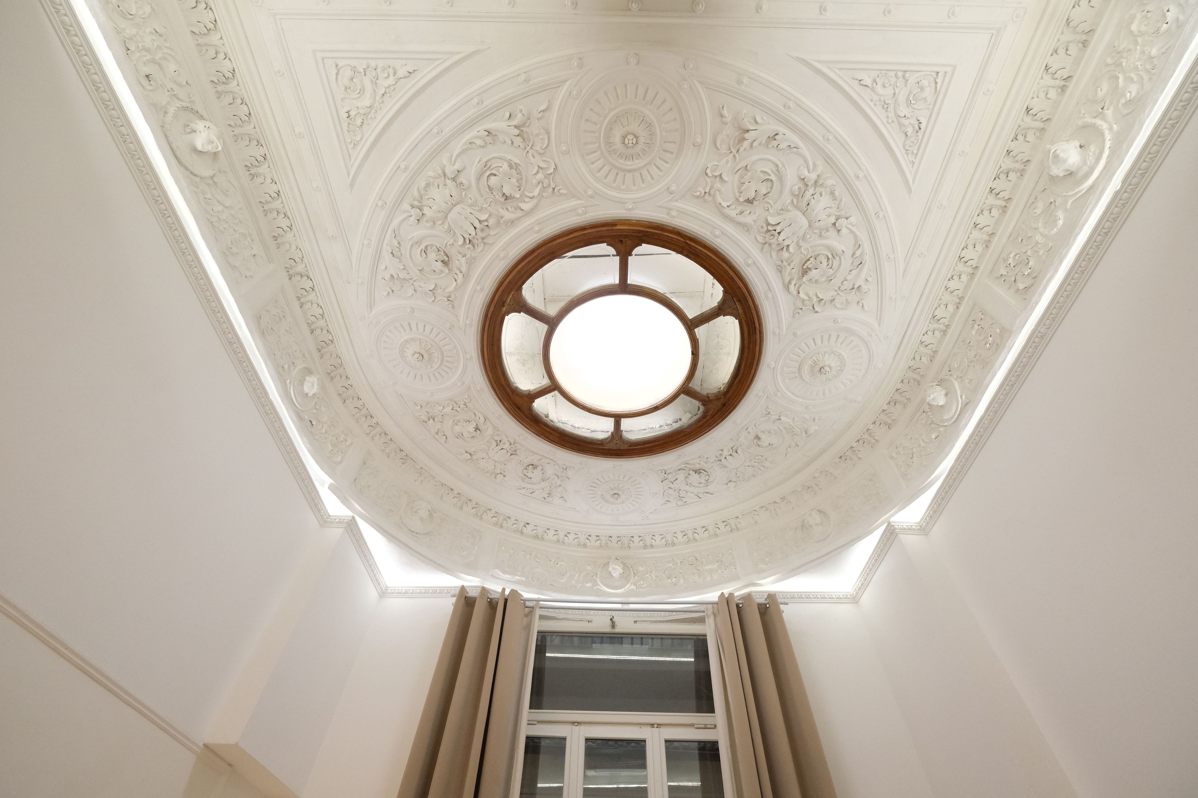 A ceiling with intricate white decorative patterns and a central circular window.