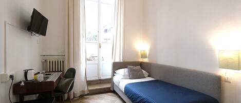Quarto com cama, escrivaninha com computador, cadeira, televisão na parede e janela com cortinas.