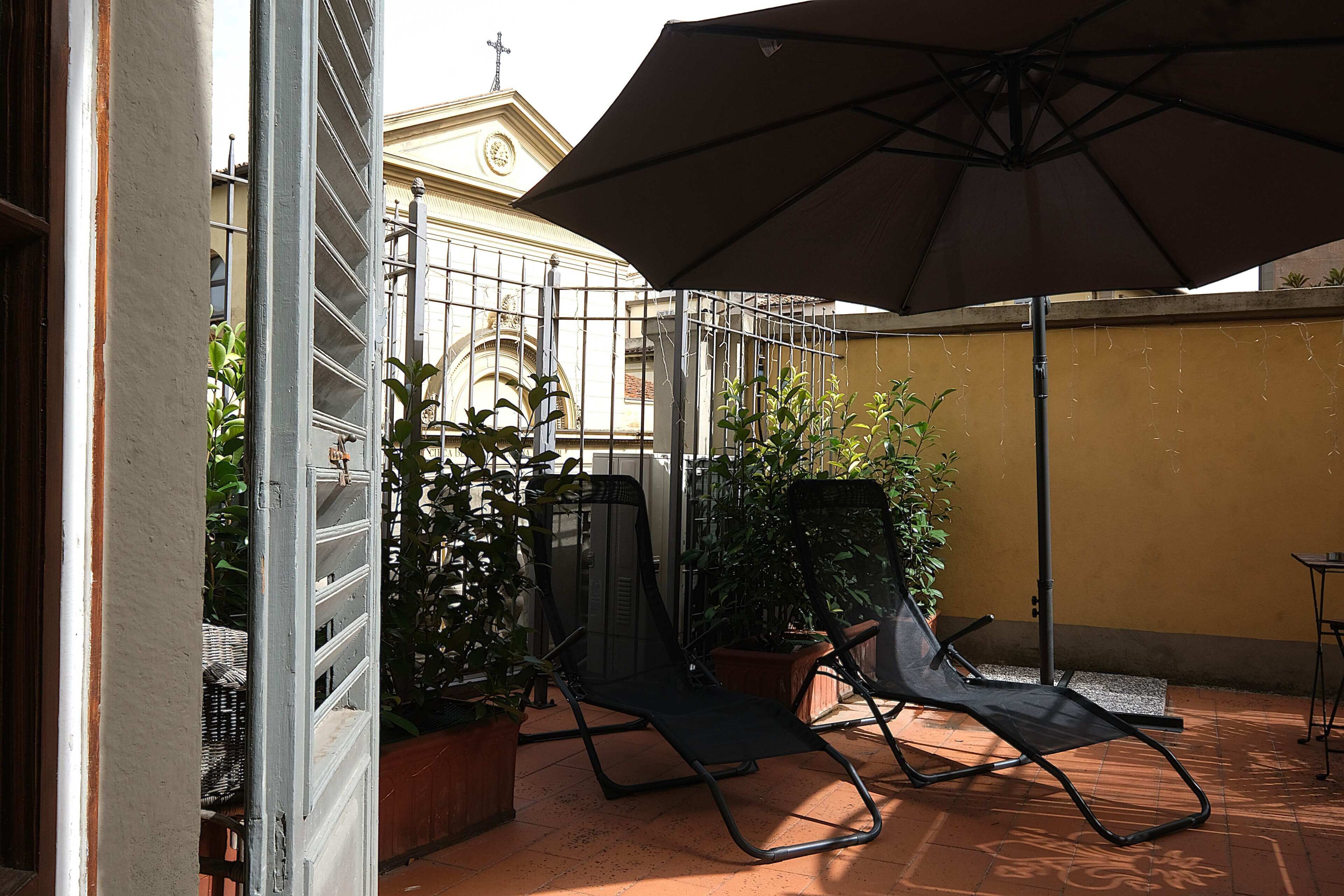 Un patio con un par de sillas, plantas en macetas y un gran parasol.