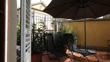 Un patio con un par de sillas, plantas en macetas y un gran parasol.