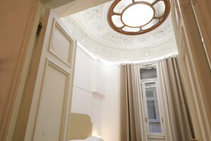 Une pièce avec un plafond haut, un décor orné au plafond, une fenêtre avec des rideaux et une porte.