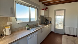 Une cuisine moderne avec vue sur la mer, des poutres en bois au plafond et une porte donnant sur un balcon.