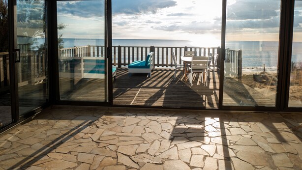 Un balcon fermé par des baies vitrées offrant une vue sur l’océan, une terrasse en bois et un espace piscine.
