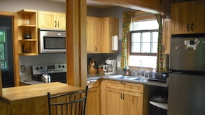 Une cuisine avec des meubles de rangement en bois, un four à micro-ondes, une cuisinière, un réfrigérateur et une fenêtre avec des rideaux.