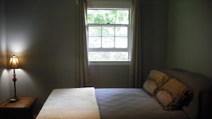 Une chambre à coucher avec un lit, une table de chevet, une lampe et une fenêtre.