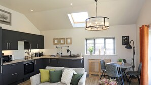 A modern kitchen with dark cabinets, a dining area with a round table, and a living room with a grey sofa. - The Tyre Barn (Whitchurch)