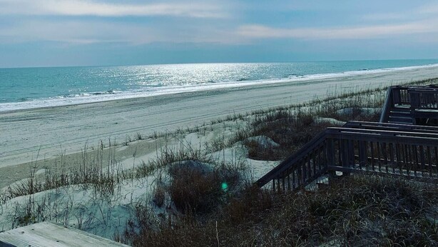 Ein Strand mit einer Holzkonstruktion im Vordergrund, einem klaren Himmel und dem Ozean im Hintergrund.