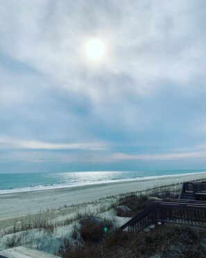 En strand med en träkonstruktion i förgrunden, en klar himmel och havet i bakgrunden.