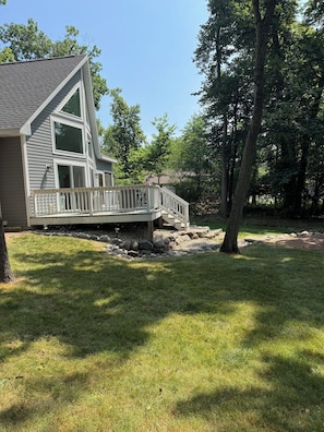 A two-story house with a deck, surrounded by a grassy yard and trees.