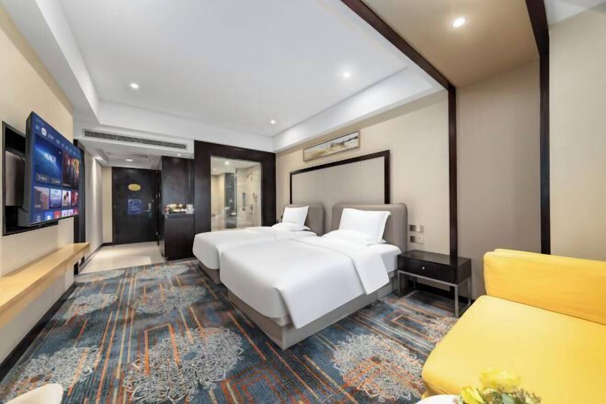 A hotel room with a large bed, a TV mounted on the wall, and a carpeted floor.